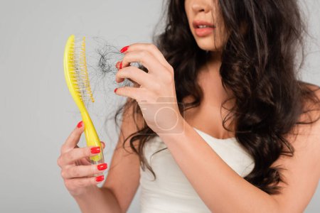Teilweise Ansicht der brünetten Frau mit Haarausfall Problem Reinigung Haarbürste isoliert auf grau