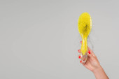 cropped view of woman with red manicure holding yellow hair brush with lost hair isolated on grey t-shirt #632785228