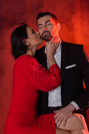brunette woman in dress seducing bearded boyfriend with closed eyes on red with smoke 