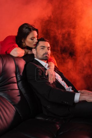 brunette woman seducing boyfriend in formal wear on red with smoke 