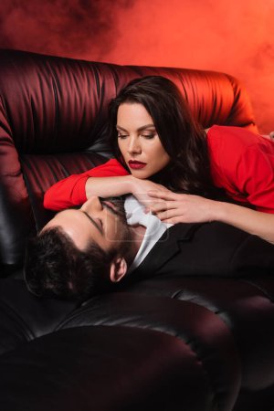 Photo for Pretty woman lying with bearded boyfriend on black couch on red with smoke - Royalty Free Image