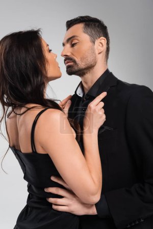 passionate woman pulling bearded man in blazer isolated on grey 