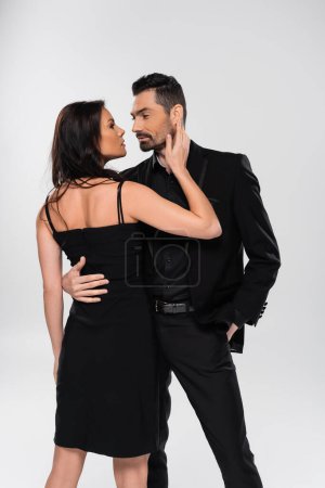 bearded man in formal wear hugging girlfriend in black dress isolated on grey 