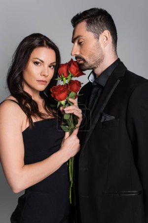 bearded man in suit near passionate woman with red roses isolated on grey