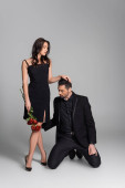 full length of dominant woman in black dress holding red roses near submissive man in suit on grey  Stickers #633165078