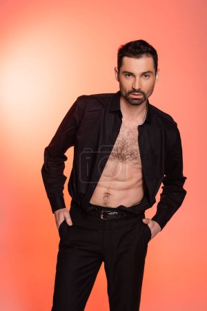 Photo for Sexy and bearded man with hairy chest standing with hands in pockets on pink - Royalty Free Image