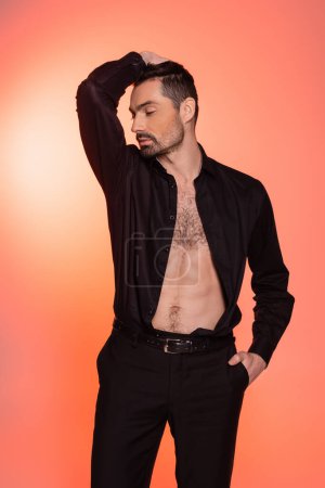 sexy and bearded man with hairy chest standing with hand in pocket on pink 