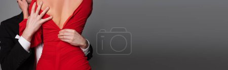 Cropped view of passionate man taking off red dress from girlfriend isolated on grey, banner 