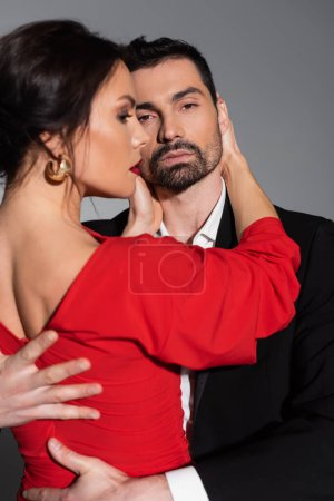 Bearded man in suit hugging blurred girlfriend in dress isolated on grey 