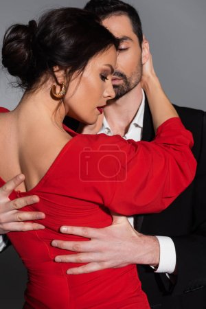Sexy woman in red dress hugging elegant man isolated on grey 