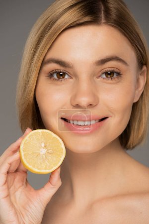 portrait of happy young woman holding organic lemon isolated on grey 