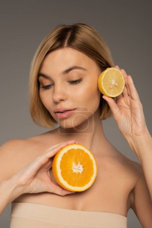 young woman holding juicy orange and sour lemon isolated on grey 