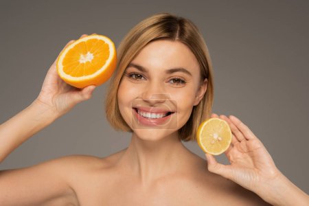 cheerful young woman holding juicy orange and sour lemon isolated on grey 
