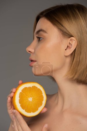 Téléchargez les photos : Profile of young blonde woman holding juicy orange half isolated on grey - en image libre de droit