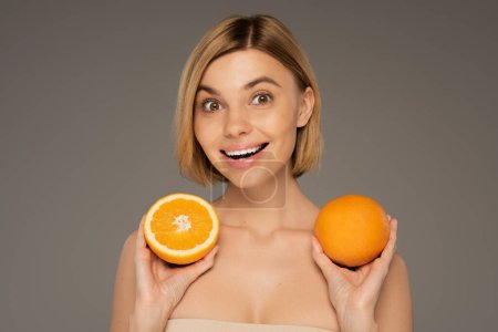 amazed young woman holding ripe oranges isolated on grey 