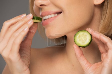 cropped view of cheerful woman holding sliced cucumbers isolated on grey 
