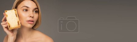Téléchargez les photos : Young woman with bare shoulders holding honeycomb isolated on grey, banner - en image libre de droit