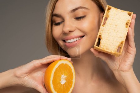happy young woman holding honeycomb and orange isolated on grey 