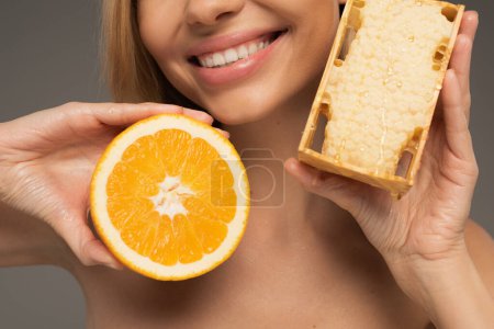 cropped view of happy woman holding honeycomb and orange isolated on grey 