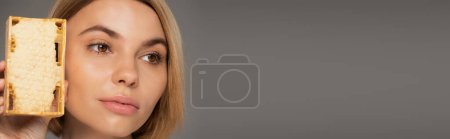 Photo for Close up of young woman holding sweet honey in honeycomb isolated on grey, banner - Royalty Free Image