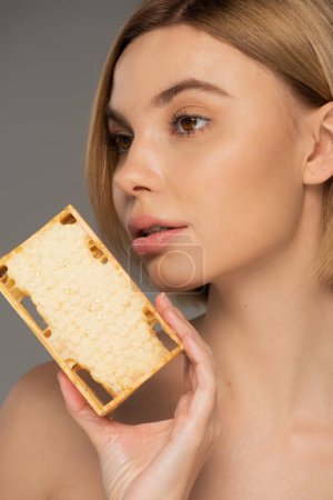 Téléchargez les photos : Close up of young woman with bare shoulder holding sweet honey in honeycomb isolated on grey - en image libre de droit
