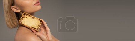 Téléchargez les photos : Cropped view of blonde young woman holding wooden frame with sweet honey isolated on grey, banner - en image libre de droit