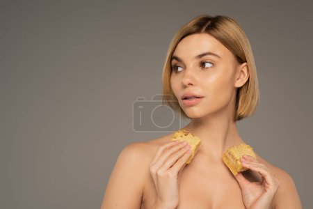 young woman with naked shoulders holding sweet honeycombs isolated on grey