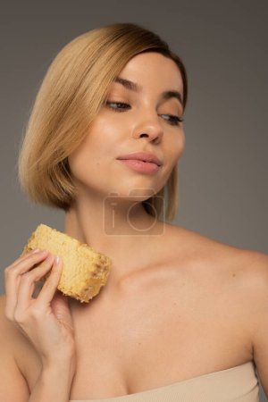 young woman holding piece of organic honeycomb isolated on grey