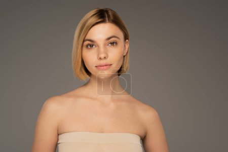 pretty woman with bare shoulders looking at camera isolated on grey 
