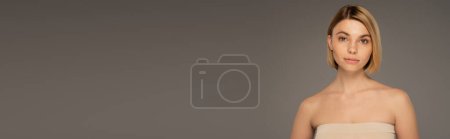 pretty woman with bare shoulders looking at camera isolated on grey, banner 