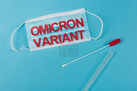 Top view of medical mask with omicron variant lettering near cotton swab on blue background 