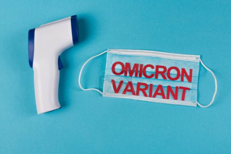 Photo for Top view of pyrometer near medical mask with omicron variant lettering on blue background - Royalty Free Image