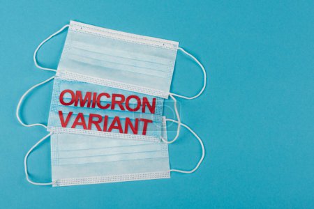 Top view of medical masks with omicron variant lettering on blue background 