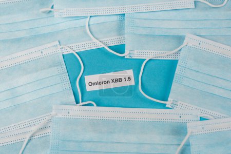 Top view of omicron xbb lettering near medical masks on blue background 