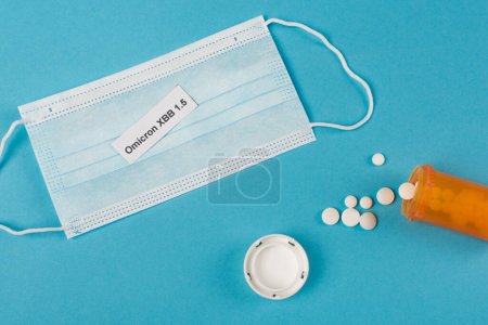 Téléchargez les photos : Top view of omicron xbb lettering on medical mask near pills on blue background - en image libre de droit