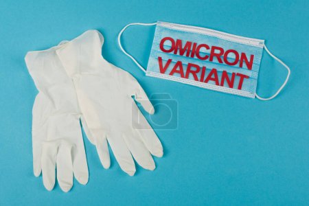 Téléchargez les photos : Top view of latex gloves near medical mask with omicron variant lettering on blue background - en image libre de droit