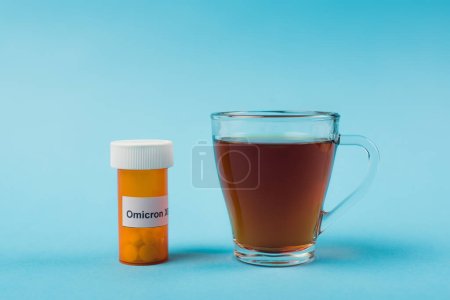 Jar with pills and omicron lettering near cup of tea on blue background 