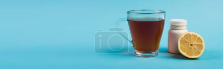Cup of tea near jar with pills and lemon on blue background, banner 