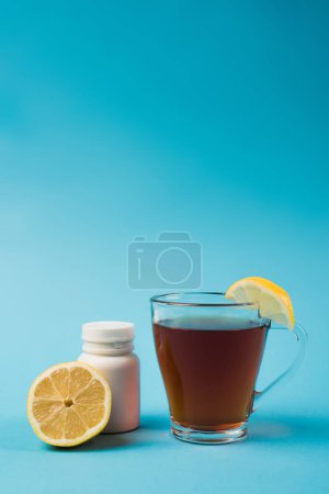 Cup of tea near lemon and cut lemon on blue background 