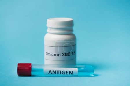 Photo for Close up view of antigen and blurred pills with omicron xbb lettering on blue background - Royalty Free Image