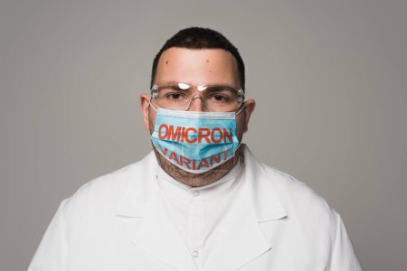 Scientist in goggles and medical mask with omicron variant lettering isolated on grey 