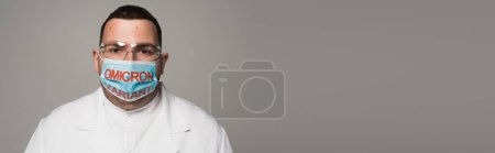 Doctor in protective goggles and medical mask with omicron variant lettering isolated on grey, banner 