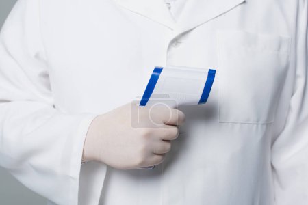 Foto de Cropped view of doctor in white coat and latex glove holding pyrometer isolated on grey - Imagen libre de derechos
