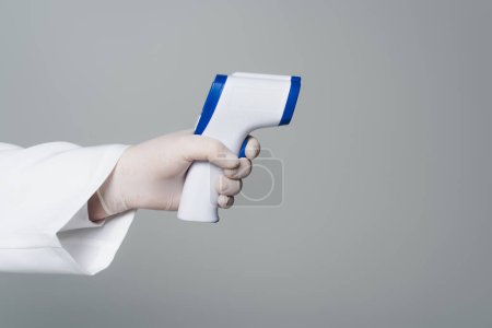 Cropped view of doctor in latex glove holding non-contact pyrometer isolated on grey 
