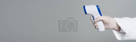 Cropped view of doctor holding non-contact pyrometer isolated on grey, banner 