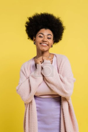 pleased african american woman with curly hair looking at camera isolated on yellow