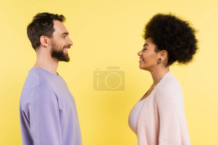 Foto de Side view of stylish african american woman and bearded man smiling at each other isolated on yellow - Imagen libre de derechos