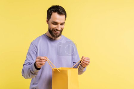 Photo for Pleased bearded man looking into shopping bag isolated on yellow - Royalty Free Image