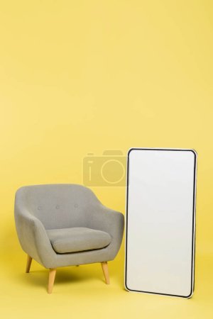 vertical view of white mock-up of mobile phone near grey armchair on yellow background