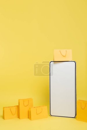 Photo for Vertical view of huge mock-up of smartphone near shopping bags on yellow background - Royalty Free Image